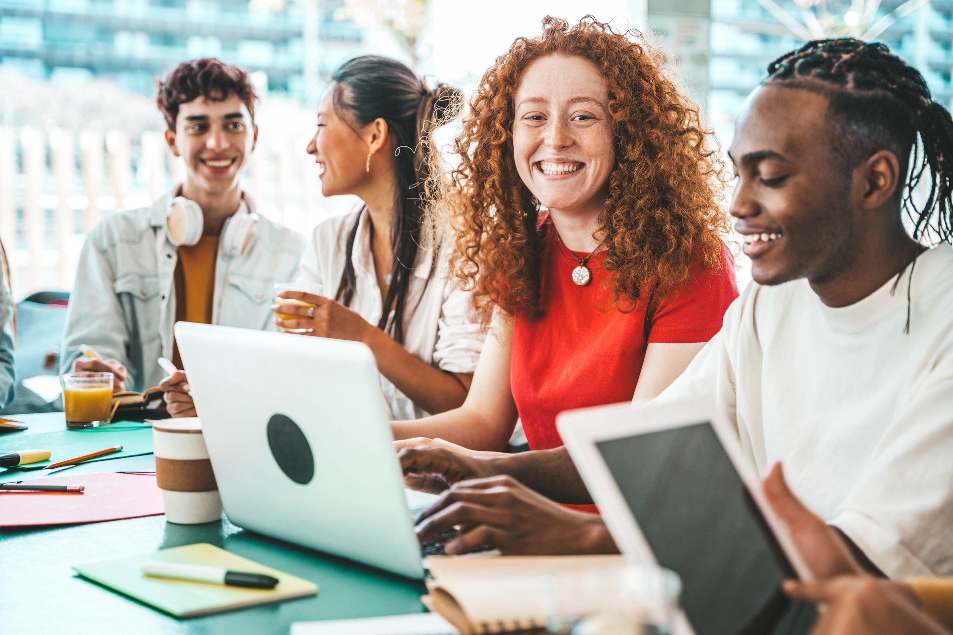 Multiracial university students sitting together at table with books and laptop - Happy young people doing group study in high school library - Life style concept with guys and girls in college campus